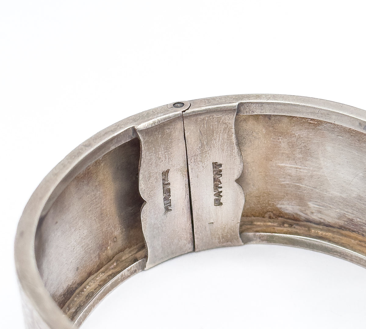Close view inside the closed cuff, where two shaped plates of the box clasp meet and small stamped letters are struck into the smooth interior surface.