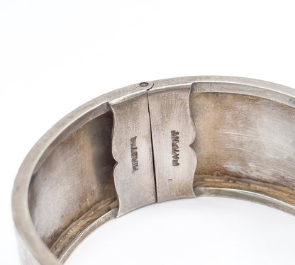 Close view inside the closed cuff, where two shaped plates of the box clasp meet and small stamped letters are struck into the smooth interior surface.