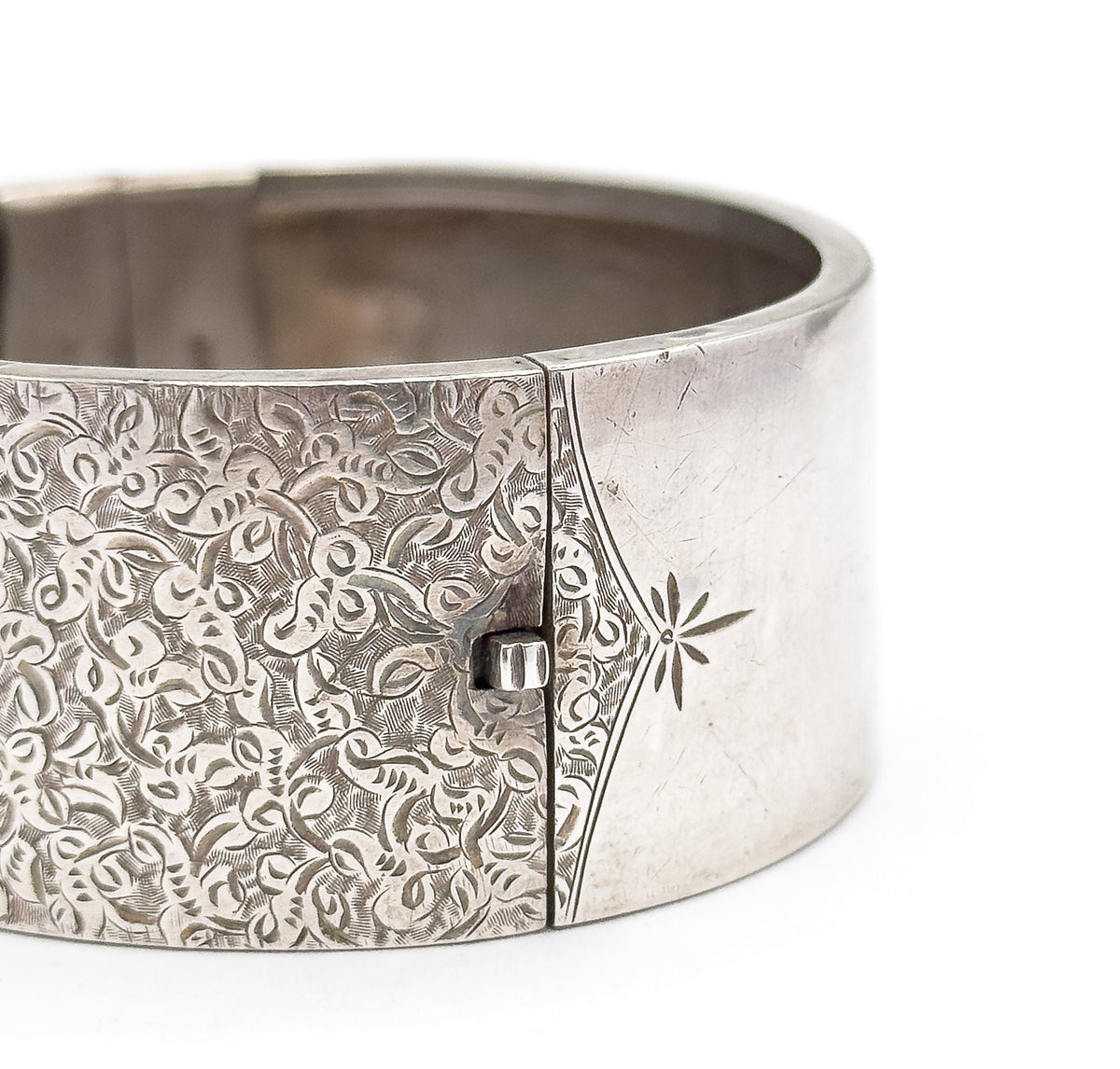 Tight outside view of the box clasp's small raised catch sitting in the seam where the ivy etching ends and the plain star-engraved panel begins, the smooth interior curving behind.