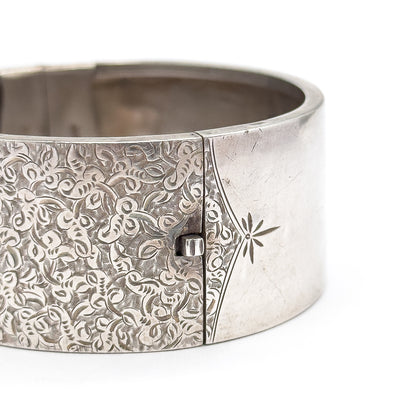 Tight outside view of the box clasp's small raised catch sitting in the seam where the ivy etching ends and the plain star-engraved panel begins, the smooth interior curving behind.