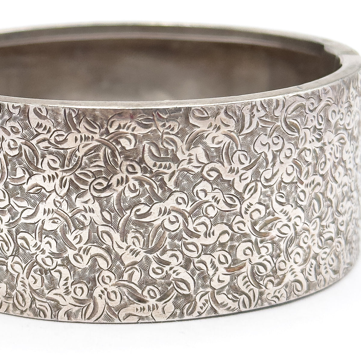 Extreme close-up of the wide band filling the frame, the dense hand-etched ivy scrolls covering the curved outer surface while the smooth interior shows past the upper rim.
