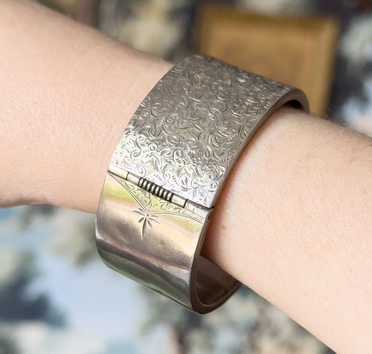 A wide Victorian hand-etched ivy cuff bracelet in sterling silver, shown on the wrist, its patterned band curving round beside a smooth polished section and the box clasp.
