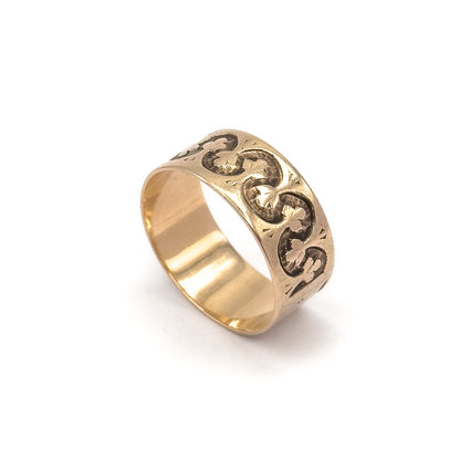 The ring stands upright at an angle against white, showing the wide band's full depth, the trefoil pattern running around the outside and the smooth polished inner shank.