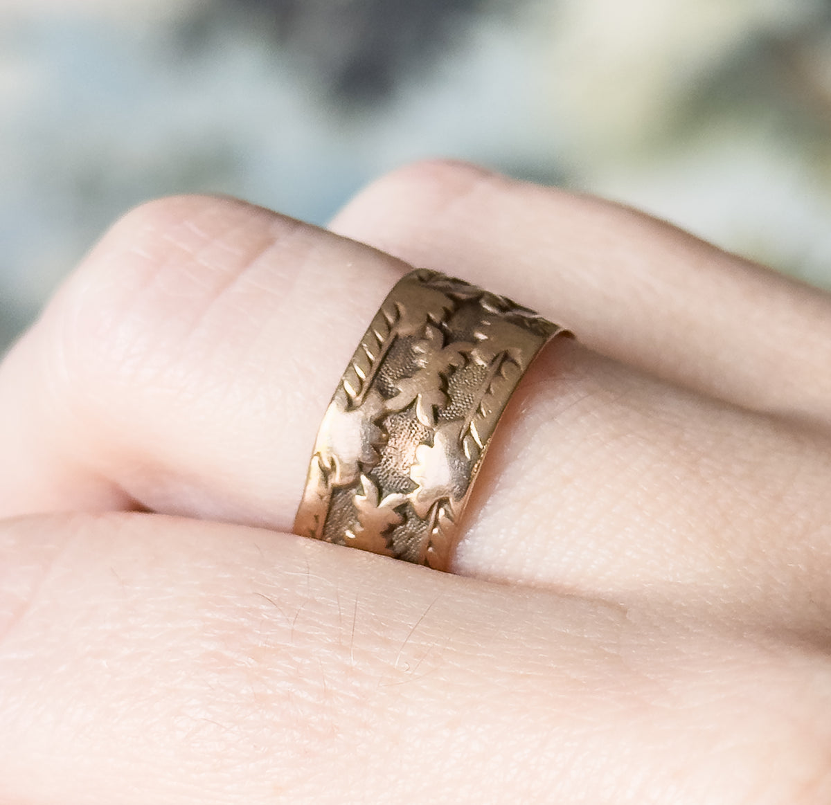 Close crop from a lower angle, showing the band sitting low against the finger with patina darkening the recesses between the carved leaves.