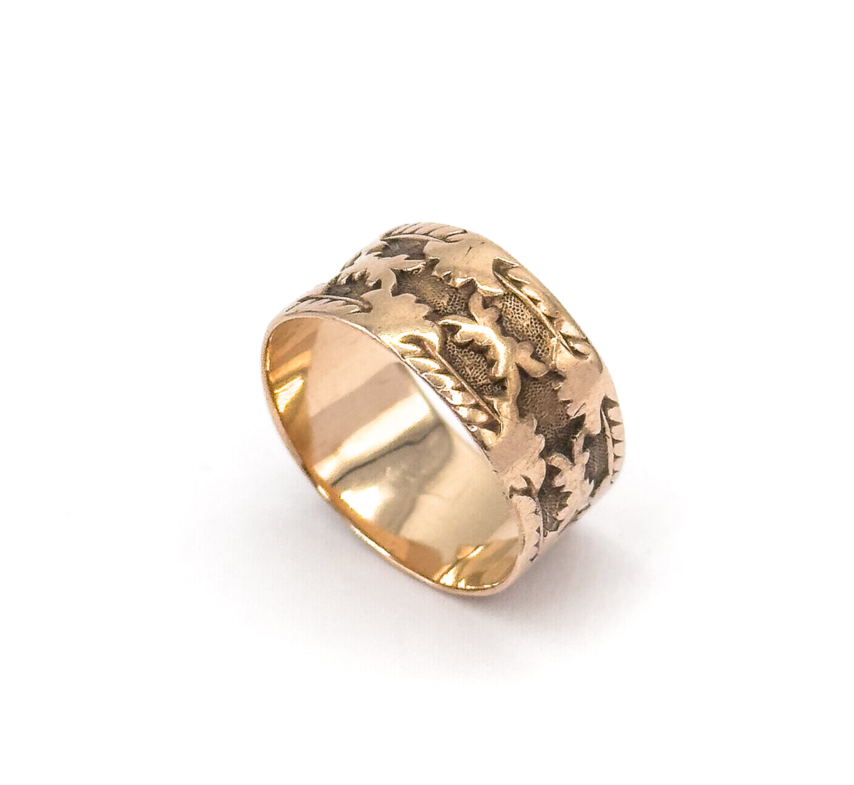 The ring alone on a plain white background, tilted so the smooth polished inside of the shank shows alongside the carved leaf pattern on the outer band.