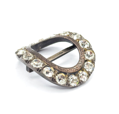 Three-quarter view from the side, the oval frame raised so the paste stones stand proud along the outer edge and the central bar crosses the open centre at a low angle.