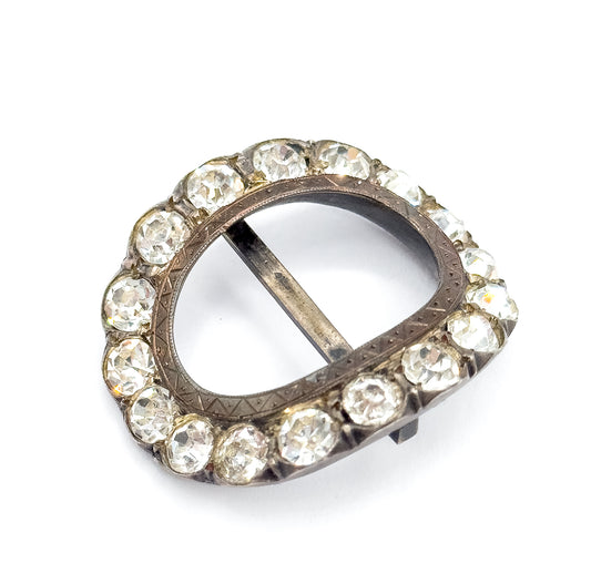 Near-overhead tilted view of the whole oval, the complete ring of colourless paste stones circling the etched frame and a small projecting tongue visible at the lower right edge.