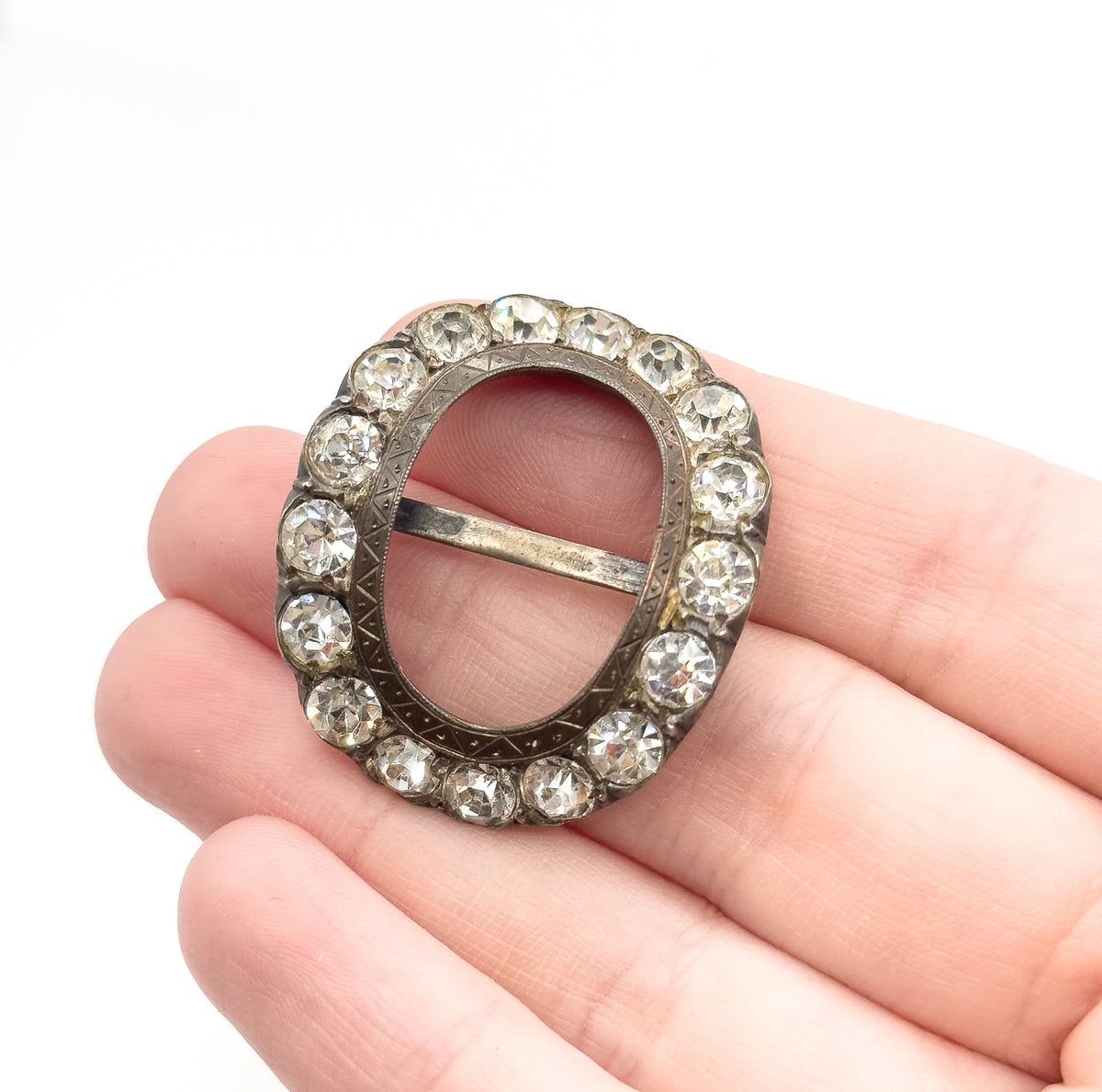 Victorian paste stone buckle in sterling silver, its oval frame ringed with colorless hand-cut paste stones and a central bar, shown resting on open fingers to convey its small size.