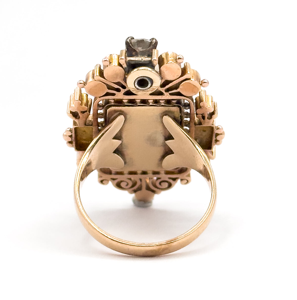 Seen from the back, the open gallery, scrolled piercing beneath the bezel and the forked shoulders where the shank meets the setting are all visible, with the prong-set diamond at the top.