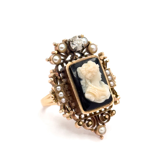 Angled three-quarter view against white, the rose gold openwork frame rising in tiers around the bezel-set cameo, with seed pearls at the corners and sides and the prong-set diamond crowning the top.
