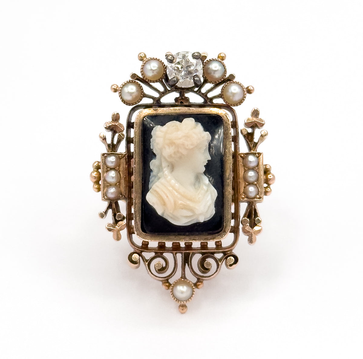 Straight-on frontal view against white, the whole face symmetrical: the prong-set diamond and fanned pearls above, the cameo centred, and a single pearl below the scrolled openwork base.