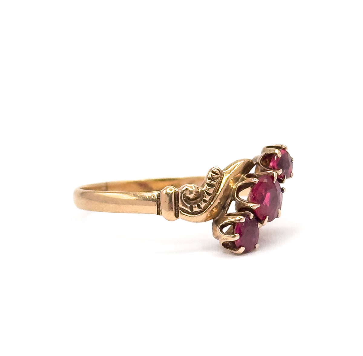 Side profile against white, showing how low the three prong-set pink tourmalines sit above the finger and how the scrolled shoulder flows into the tapering shank.