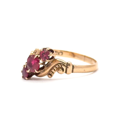 Close side view from the opposite end, the scrolled shoulder detail and prong tips in sharp focus while the three pink tourmalines angle away to the left.