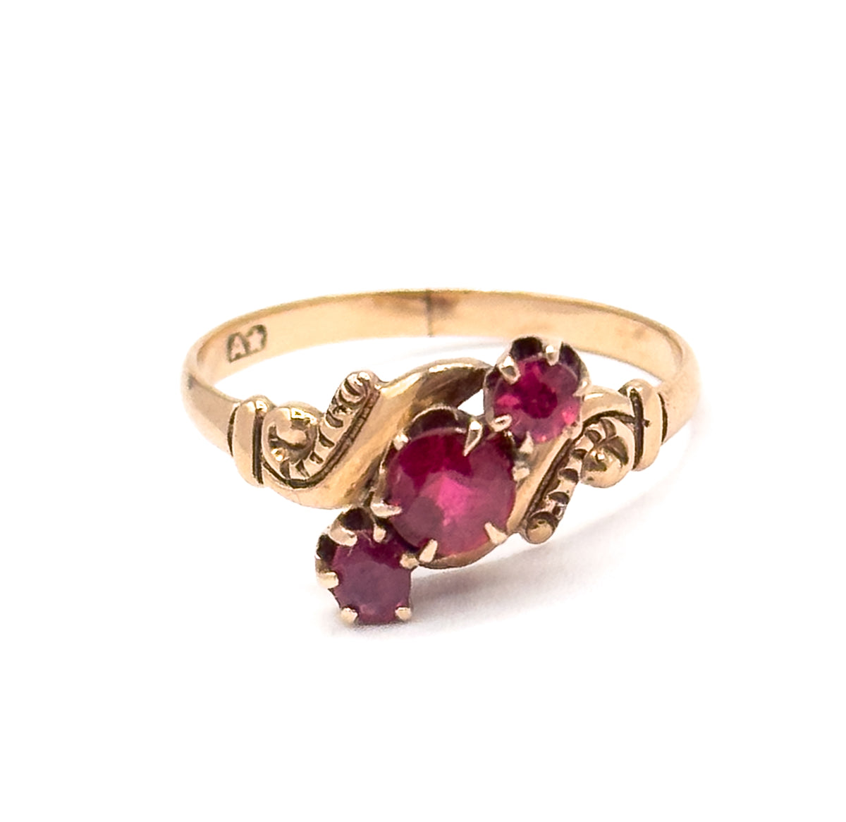 Three-quarter front view with the ring upright, showing all three prong-set pink tourmalines stepped diagonally across the face between scrolled shoulders, with a small stamped mark on the inner shank.