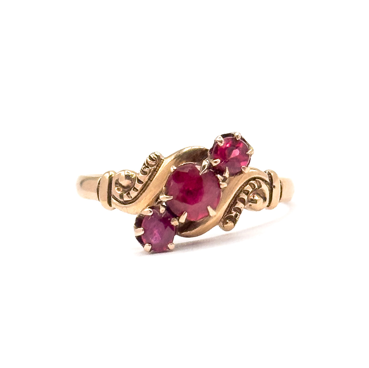 Head-on view from the front with the face tilted toward the camera, the central pink tourmaline largest between its two smaller prong-set accents, scrolled shoulders sweeping out either side.