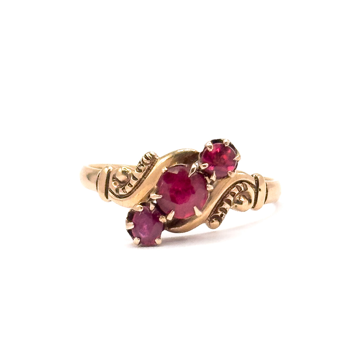 Victorian pink tourmaline trilogy ring in rose gold, shown upright at an angle against white, its three round prong-set stones set diagonally between scrolled shoulders.