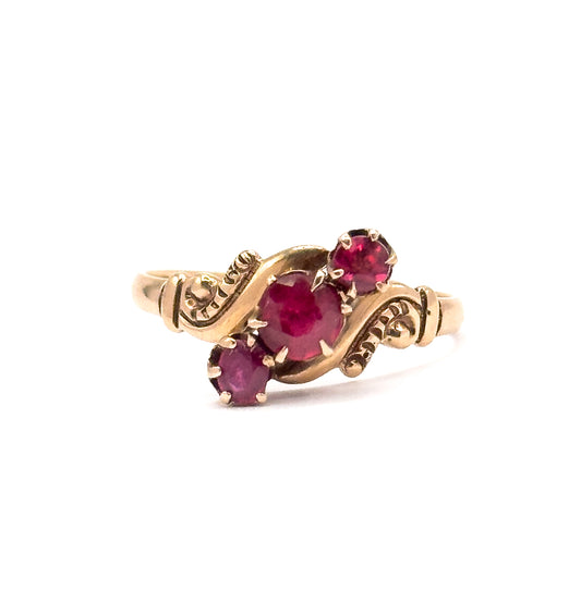 Victorian pink tourmaline trilogy ring in rose gold, shown upright at an angle against white, its three round prong-set stones set diagonally between scrolled shoulders.