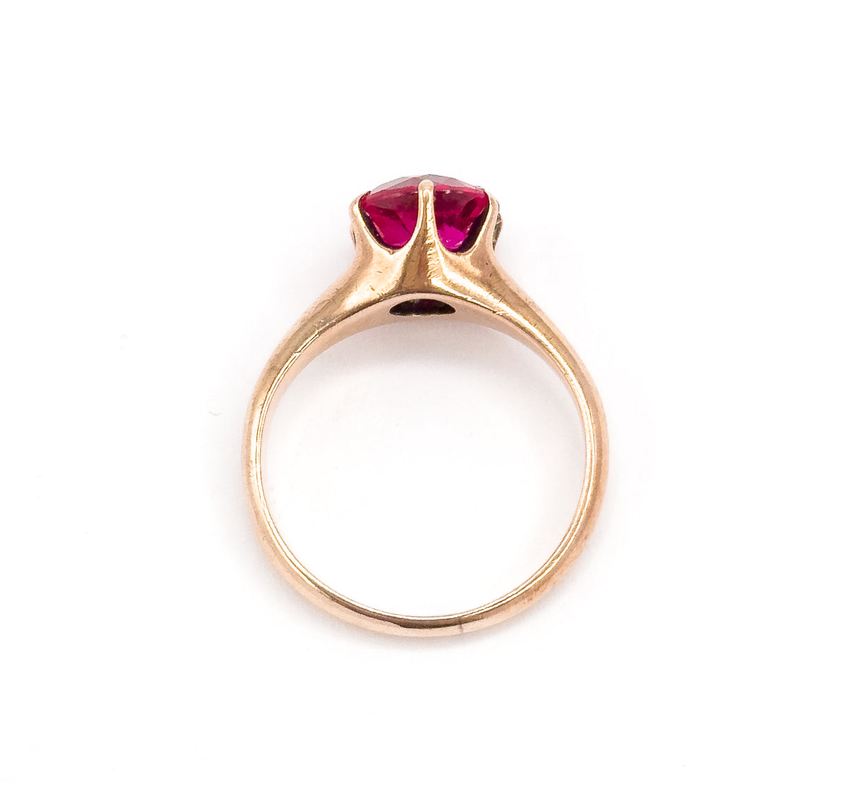 Looking straight through the circle of the shank, the open band framed against white with the bright pink stone visible in its prongs at the top and the setting's underside open beneath.
