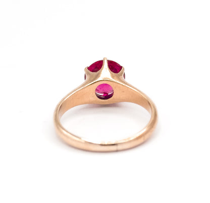 Rear view with the rose gold shank standing upright, showing the open underside of the setting where the bright pink stone shows through a round window below the prongs.