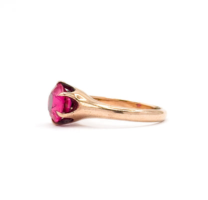 Profile view against white, the rose gold shank sweeping up into a tapered shoulder and curved prong gripping the bright pink round stone from the side.