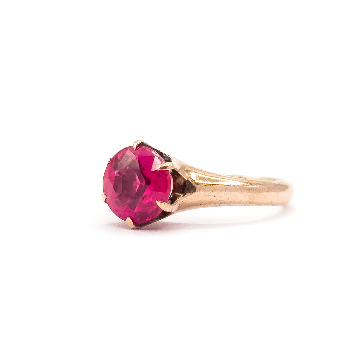 Three-quarter side angle with the stone's facets tilted toward the viewer, the prongs curling over its edge and the rose gold shoulder flowing back into the narrow shank.