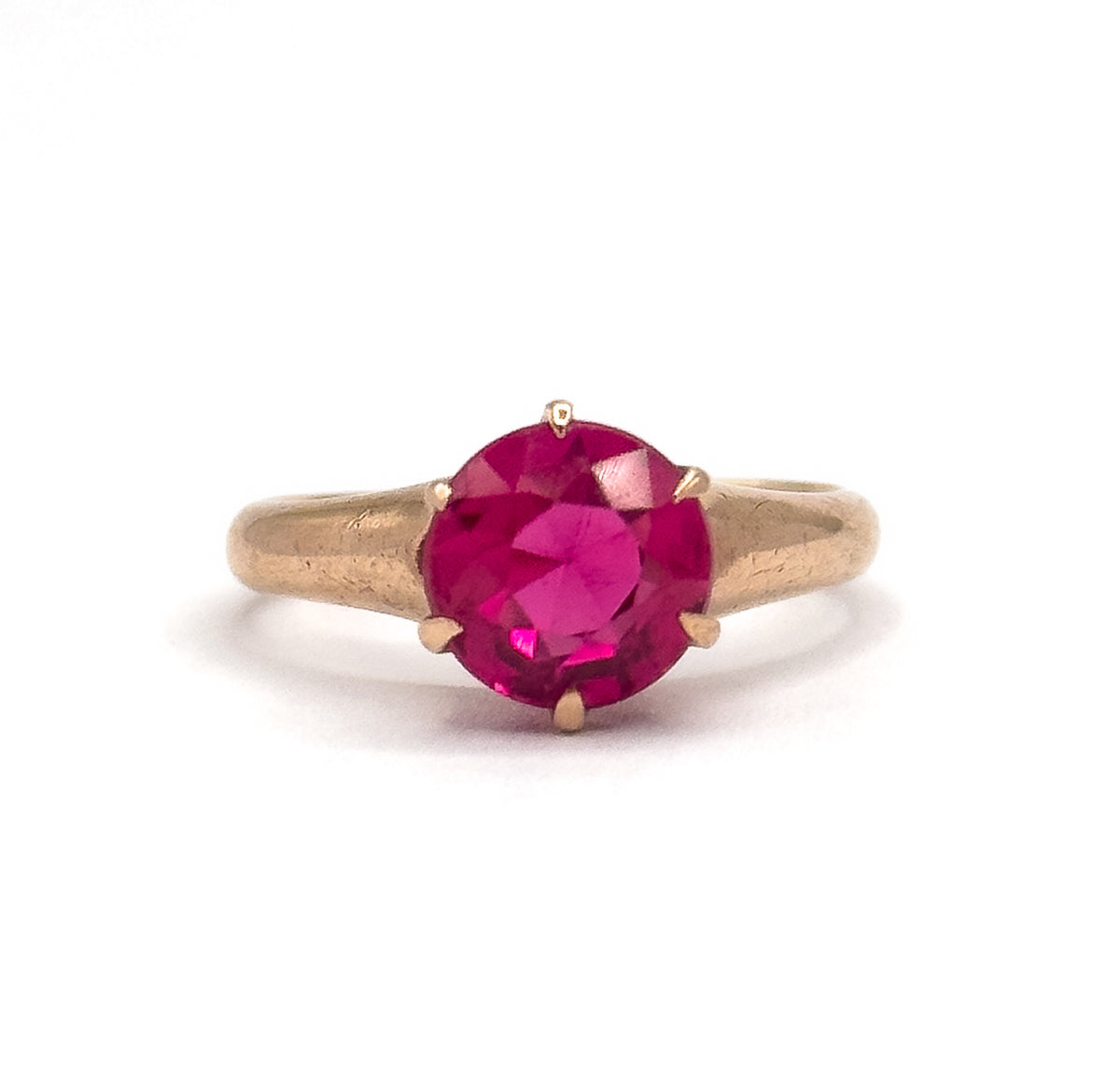 Top-down view with the round bright pink stone facing the camera, six prongs spaced around its edge and the rose gold shoulders tapering away to each side.