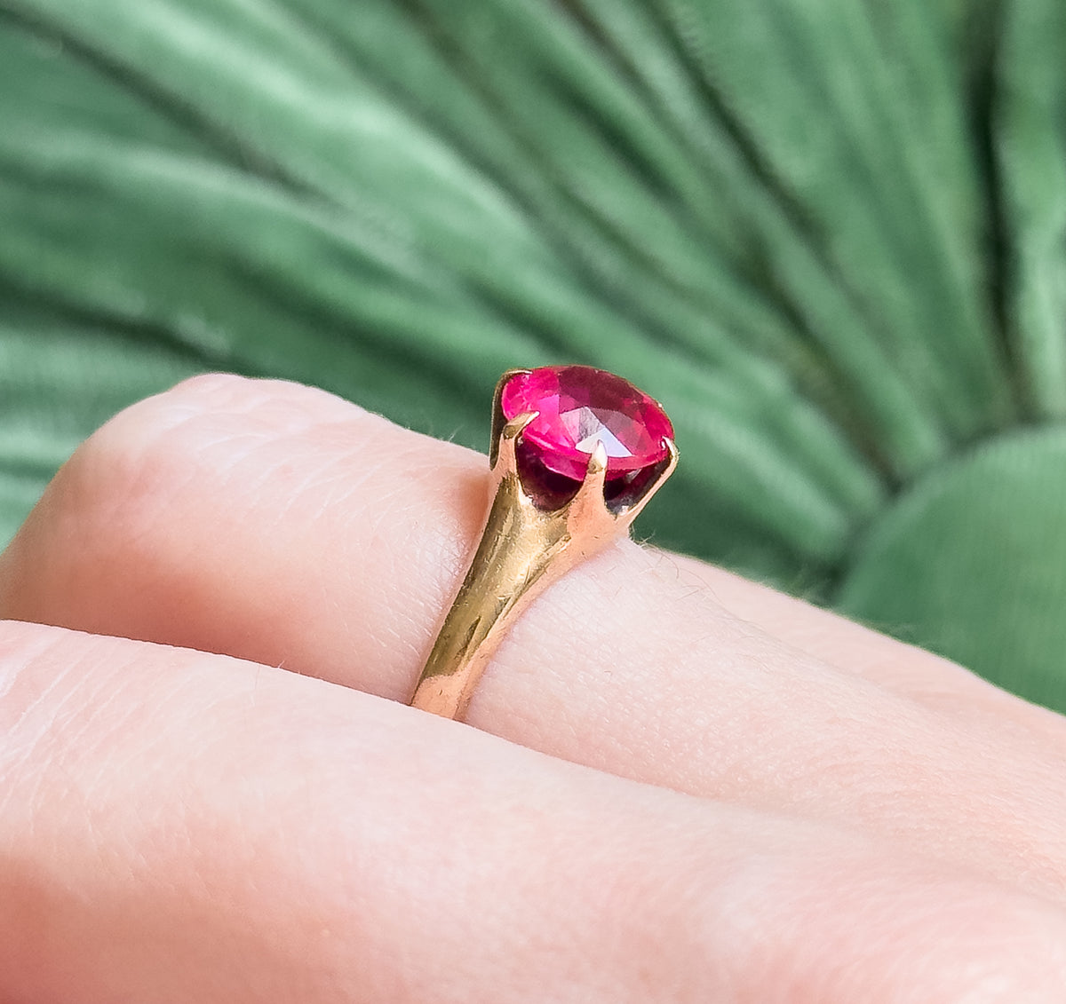 Shown on a finger against soft green, this close view gives a sense of scale as the rose gold setting lifts the bright pink round stone above the knuckle.