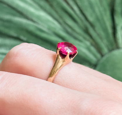 Shown on a finger against soft green, this close view gives a sense of scale as the rose gold setting lifts the bright pink round stone above the knuckle.