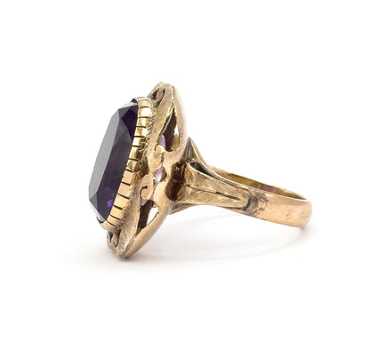 Full side view from the left, where the ridged bezel wall rises in profile to show how tall the purple stone sits above the finger, with textured shoulders flowing into the shank.