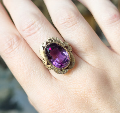 Viewed from above on the finger, the amethyst's deep purple fills the oval bezel while the scalloped gold face spans the full width of the finger between the knuckles.