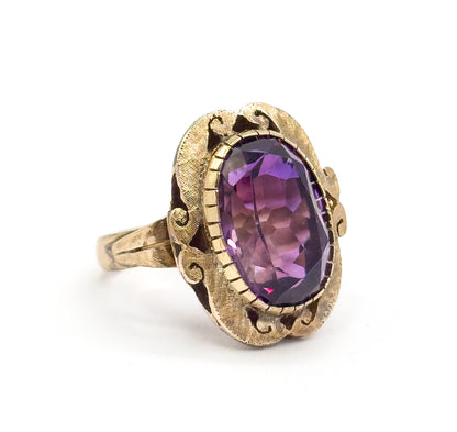 Off the hand against plain white, the ring stands in three-quarter profile so the raised oval bezel, scrolled cutouts beneath it and the narrowing textured shank are all visible.