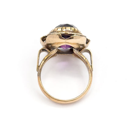 Seen end-on from behind, the open gallery shows purple glowing through the pierced cutouts beneath the bezel as the yellow gold shank sweeps down in a smooth circle.