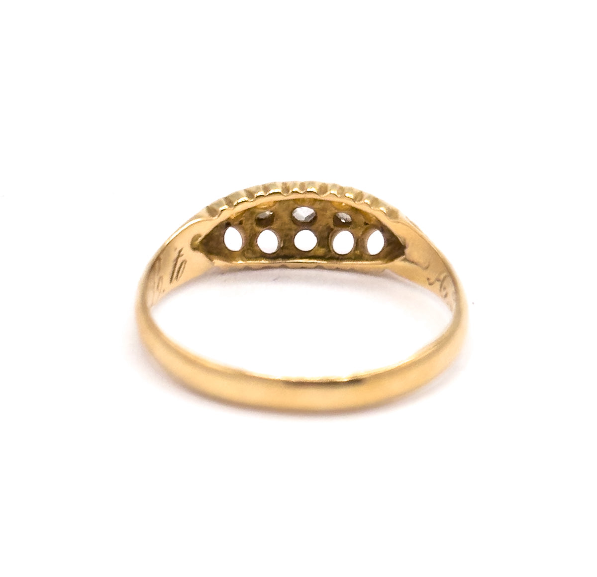 Rear view of the setting's underside, where five round openings in the yellow gold gallery show the backs of the diamonds, with script engraving curving along the inner shank beneath.