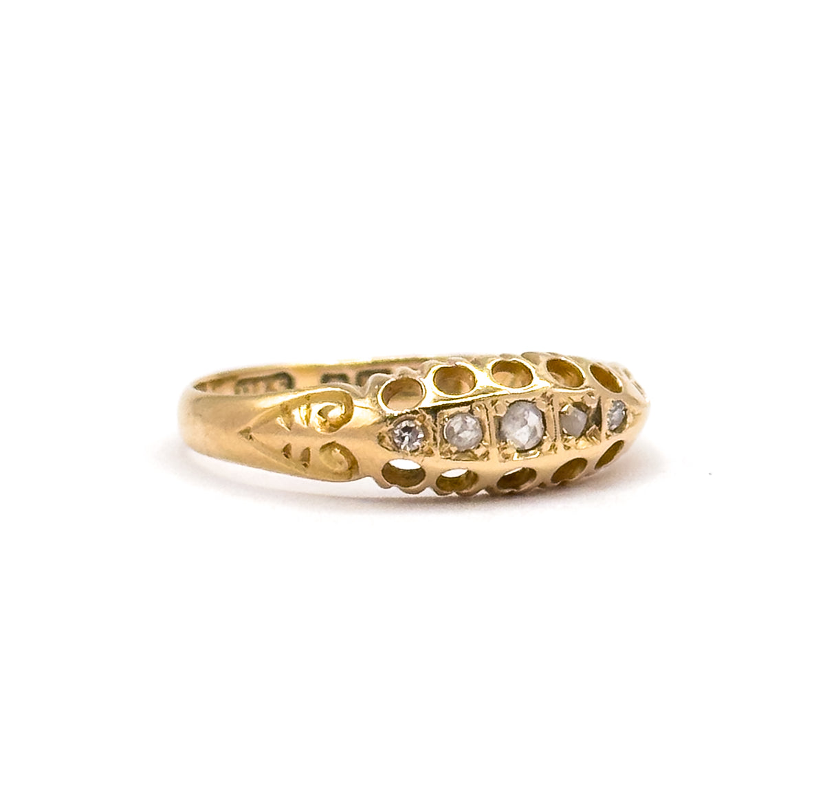 Side-on view across the face where all five graduated round diamonds sit in a row, with pierced openings along the yellow gold gallery and a scrolled shoulder leading into the tapered shank.