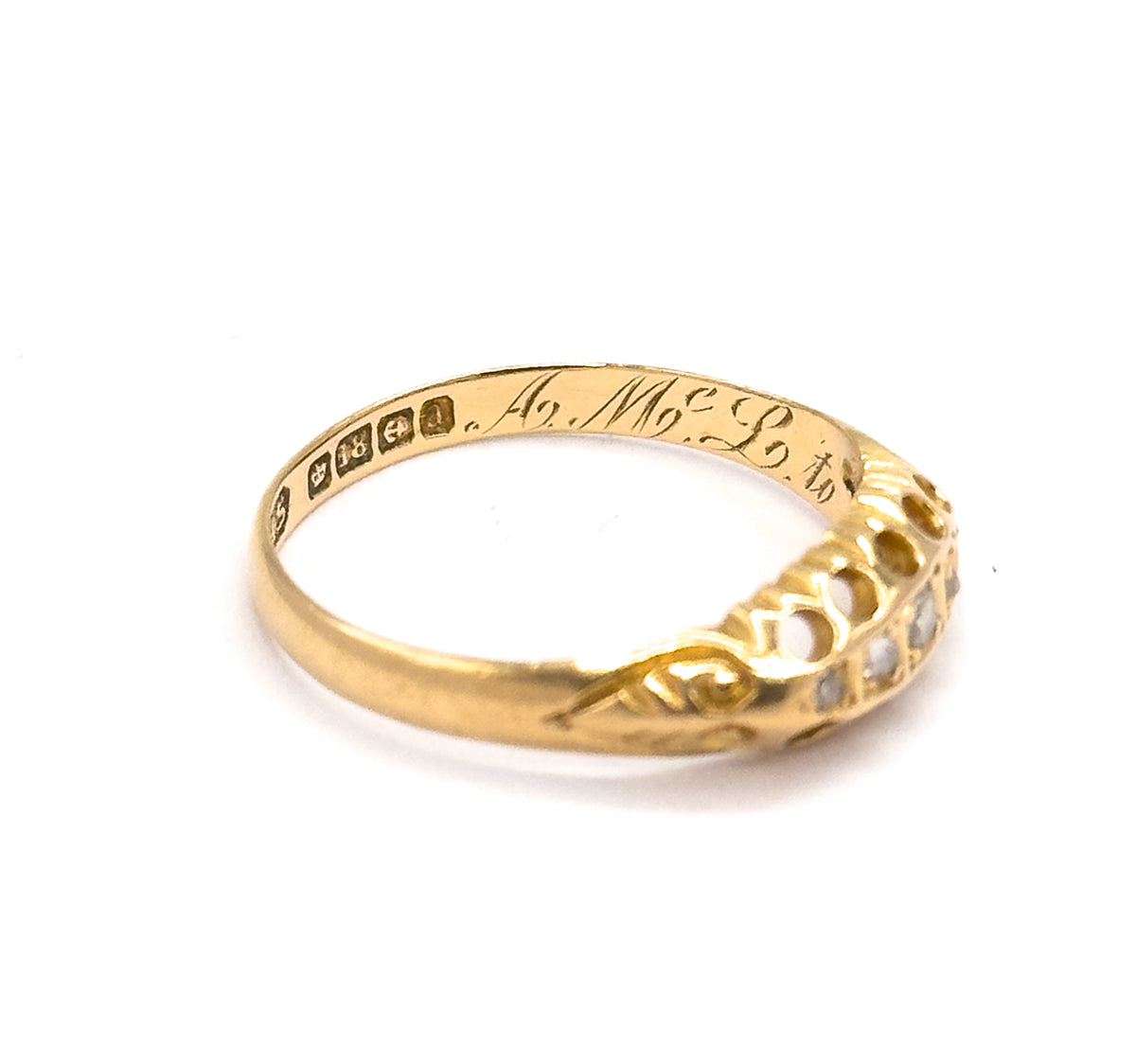 Close view inside the band where a line of small stamped hallmark punches sits beside the flowing script initials engraved on the inner shank, the diamond setting angled away at the right.