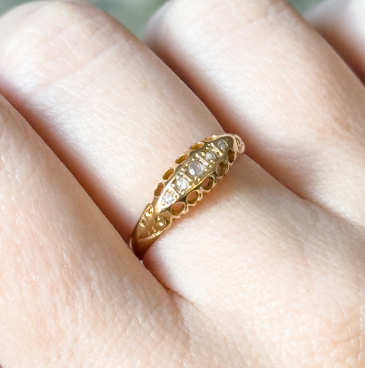 Edwardian five-stone diamond ring in 18K yellow gold, shown on a finger in close-up, its graduated row of small diamonds set along a tapering, low-profile band.