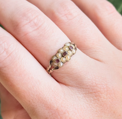 Shown on a finger from above with the hand filling the frame, the face reading as rows of small pearls set around two deep pinkish-purple tourmalines, the band sitting low against the skin.