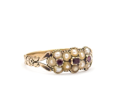 Georgian seed pearl and tourmaline floral ring shown upright in profile against white, its pearl clusters framing pinkish-purple tourmalines, with carved leaf-like split shoulders along the shank.