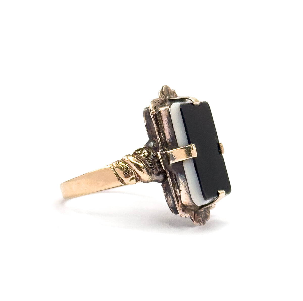 Side profile against white, showing how low the sardonyx tablet sits above the finger, with flat prongs gripping the stone's edge and the scrolled shoulder flowing into the slim shank.