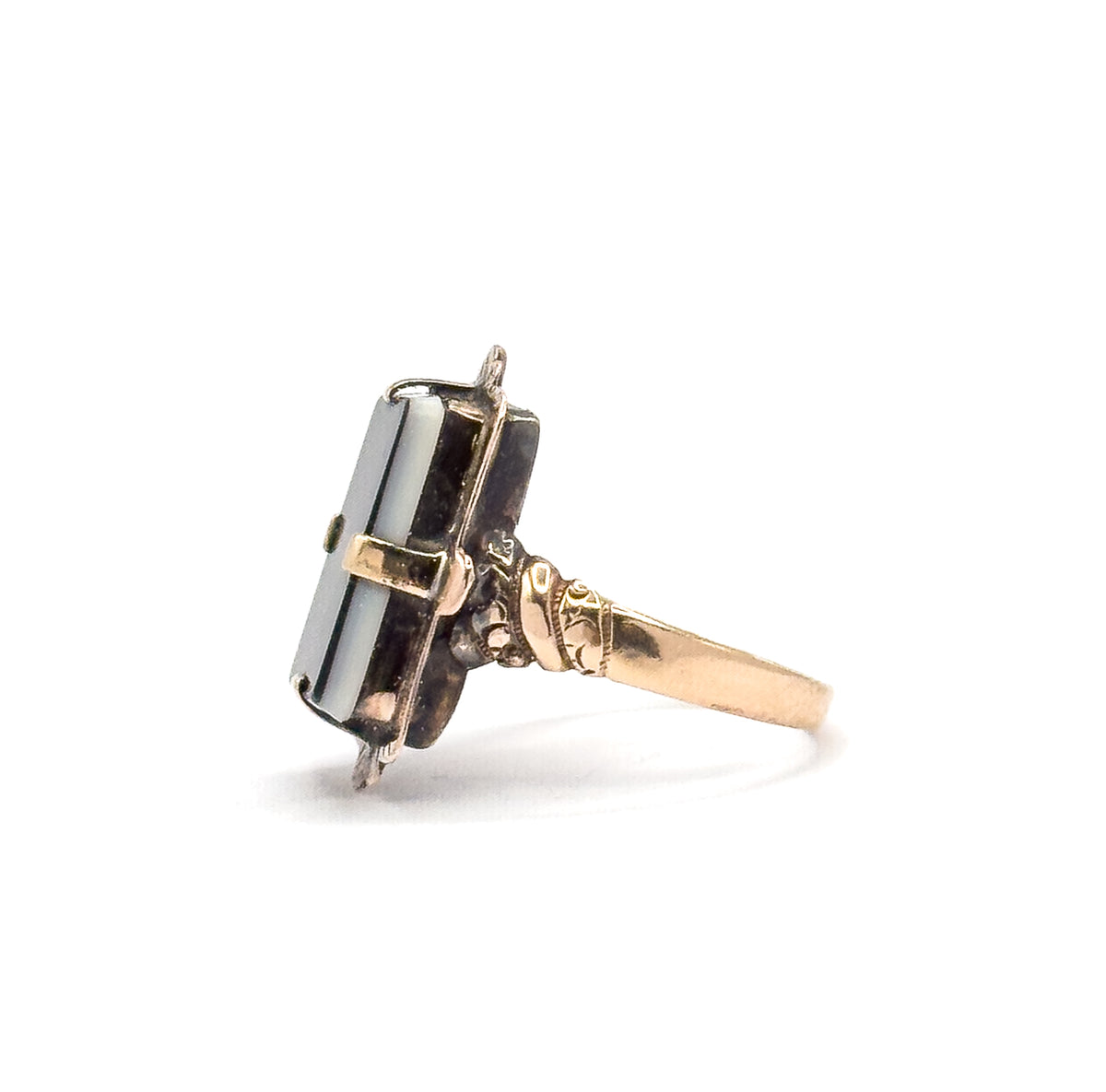 Side profile against white, showing how low the sardonyx tablet sits above the finger, with the prong tips folded over its edge and the shoulder tapering into the slim shank.
