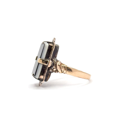 Side profile against white, showing how low the sardonyx tablet sits above the finger, with the prong tips folded over its edge and the shoulder tapering into the slim shank.