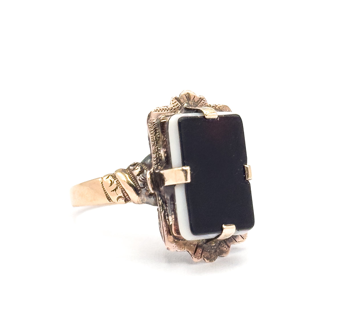 Victorian sardonyx hardstone ring in gold, shown upright at an angle against white, the rectangular black-and-white stone held by prongs in a decorative mount above a tapering shank.