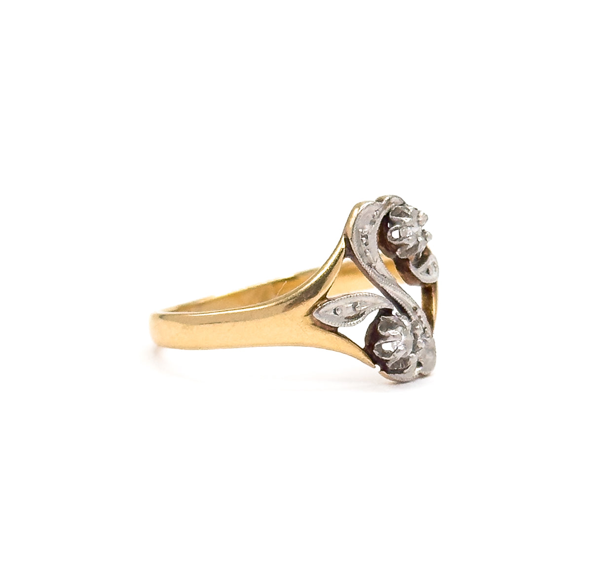 Side profile against white, showing how the yellow gold shank tapers and sweeps up into the low white gold "S" face, with the two prong-set diamonds seen edge-on.