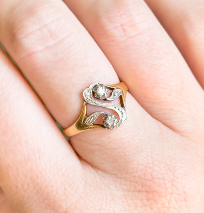 Almost the same view with slightly different angle, the ring shown on a finger tilted so light catches both prong-set diamonds and the milgrain scrolls of the white gold "S" face.