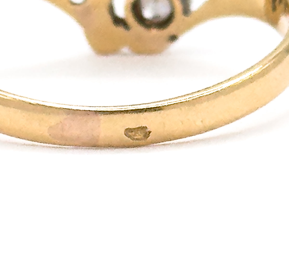 Extreme close-up of the outer shank, where a small hallmark punch is struck into the yellow gold band, the diamond-set face blurred above.