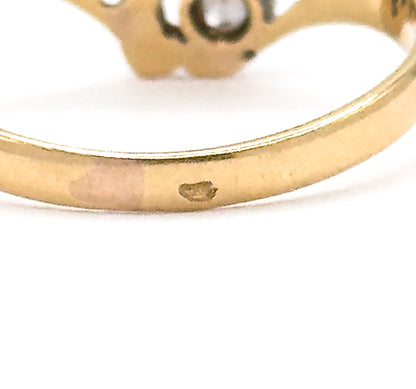 Extreme close-up of the outer shank, where a small hallmark punch is struck into the yellow gold band, the diamond-set face blurred above.
