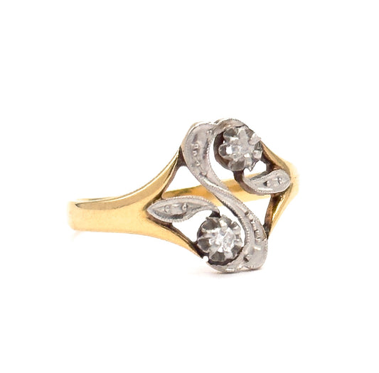 Art Nouveau moi et toi ring in 18K yellow gold, shown upright against white, its two prong-set single-cut diamonds in a white gold "S"-shaped face with openwork and milgrain detail.