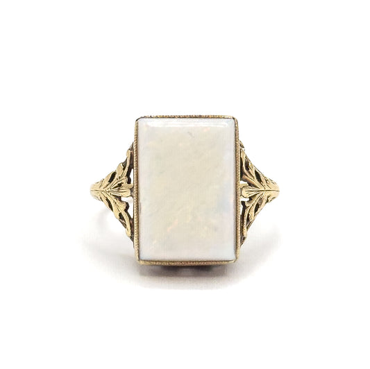 Standing upright and photographed straight on, the rectangular opal faces the viewer within its bezel, flanked by symmetrical pierced leaf shoulders that taper into the shank below.