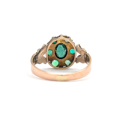 Upright from behind against white, the back of the oval bezel fills the frame with the green stones and seed pearls visible through their openings above the curved shank.