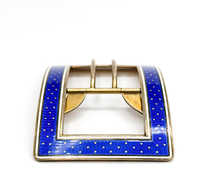 Head-on view of the enamelled face with the twin pin prongs rising above the notched crossbar, the blue guilloché and white enamel borders framing the open rectangle on all four sides.
